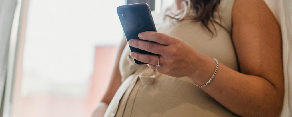 An image taken of a pregnant woman. she is pictured looking at her mobile phone.