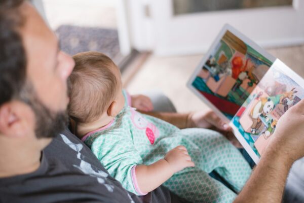 An image taken of a male reading a book to a baby.