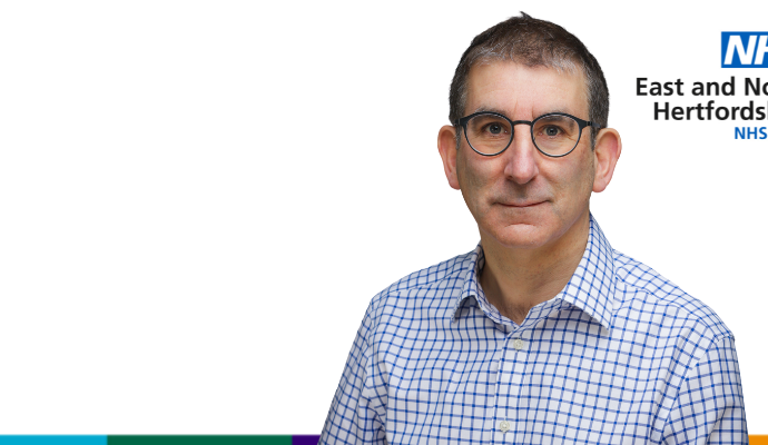 A white background with a man (Justin Daniels) wearing a plaid shirt in the foreground. Justin is smiling, wearing glasses with short hair.